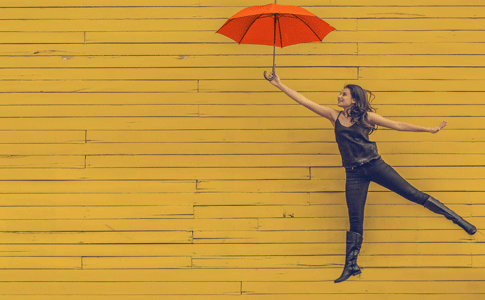 bookmans east women girl holding orange umbrella against yellow background like she's flying away